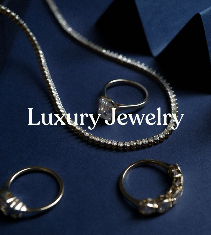 Luxury Jewelry: sparkling gemstone rings and a necklace displayed on dark blue fabric.