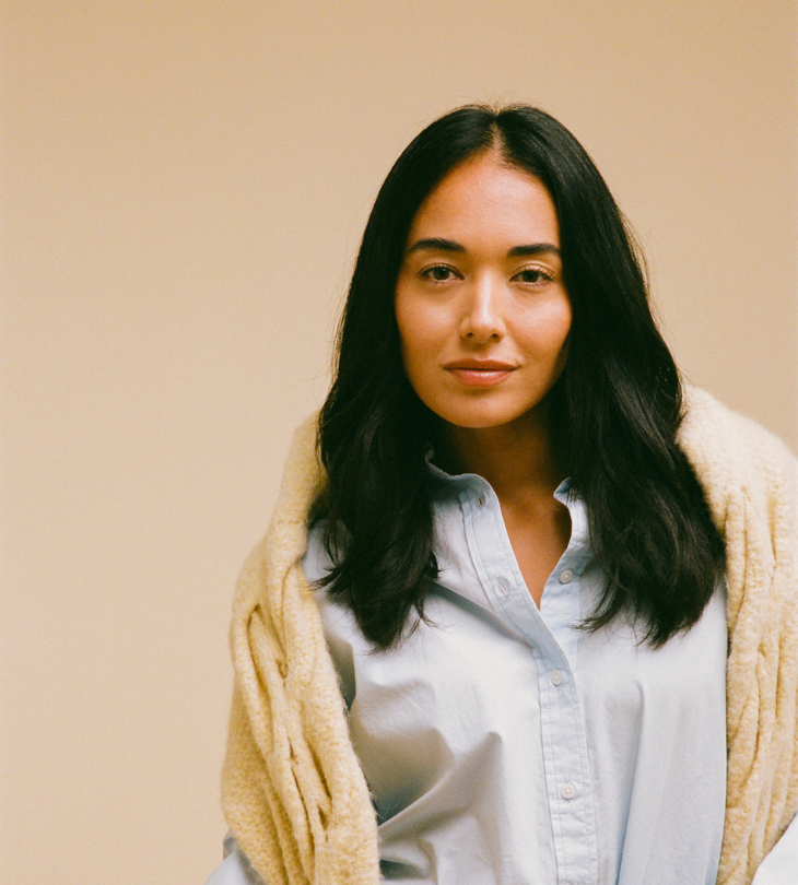 Woman wearing a light-colored cardigan over a white shirt against a beige background