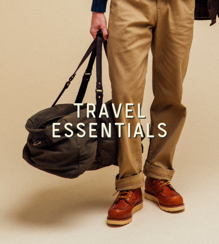 Person holding a duffel bag with 'TRAVEL ESSENTIALS' text on a beige background
