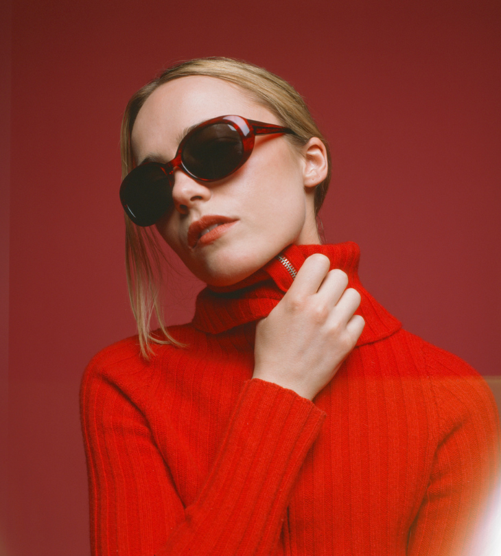 Person wearing a red turtleneck sweater and sunglasses against a red background