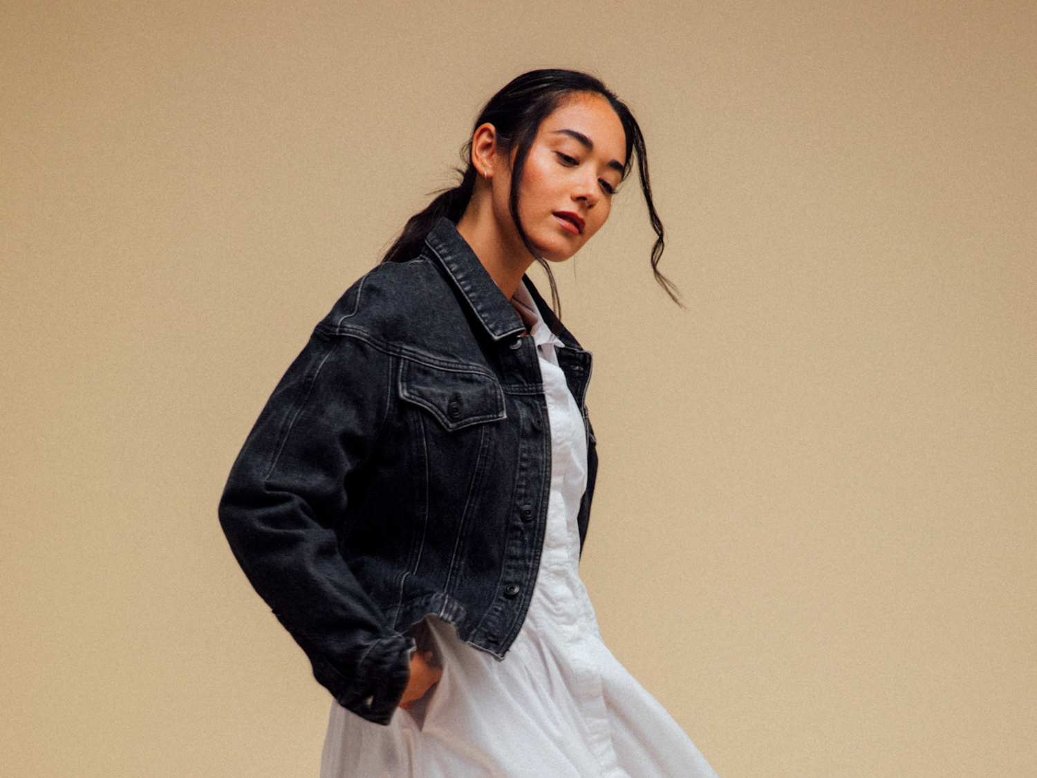 Woman wearing a black denim jacket over a white dress on a beige background