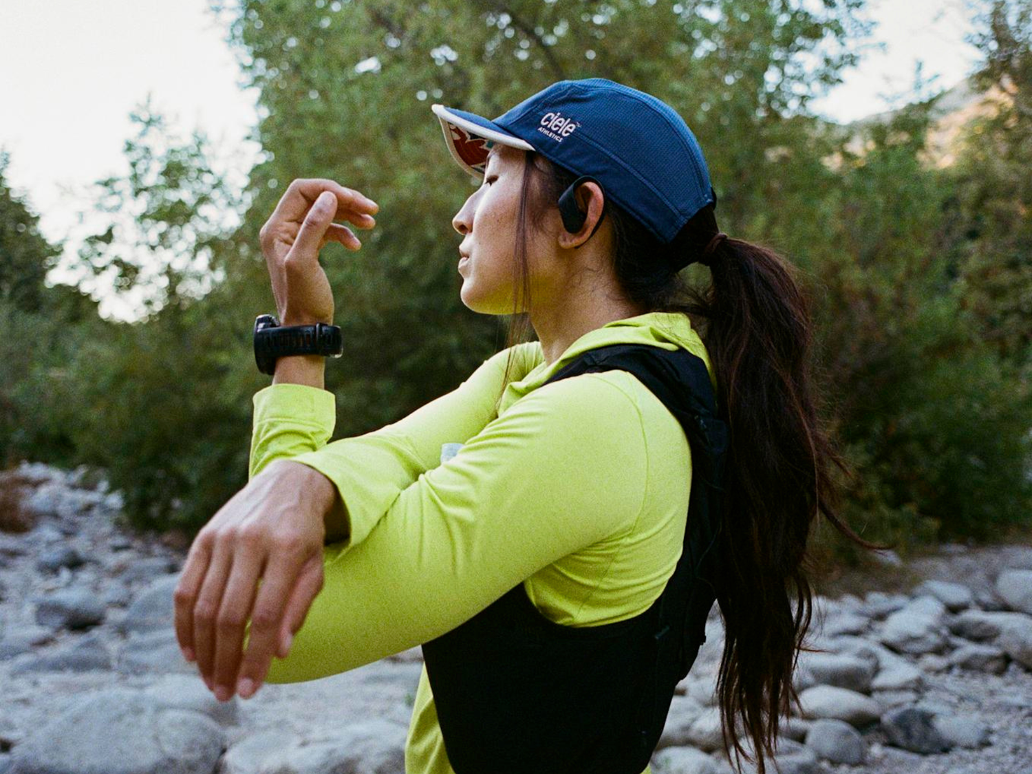 Woman in athletic wear with a cap and watch, outdoors on a rocky path.