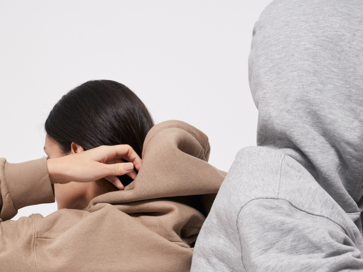 Two people wearing hoodies, one in brown and the other in gray, against a plain background.