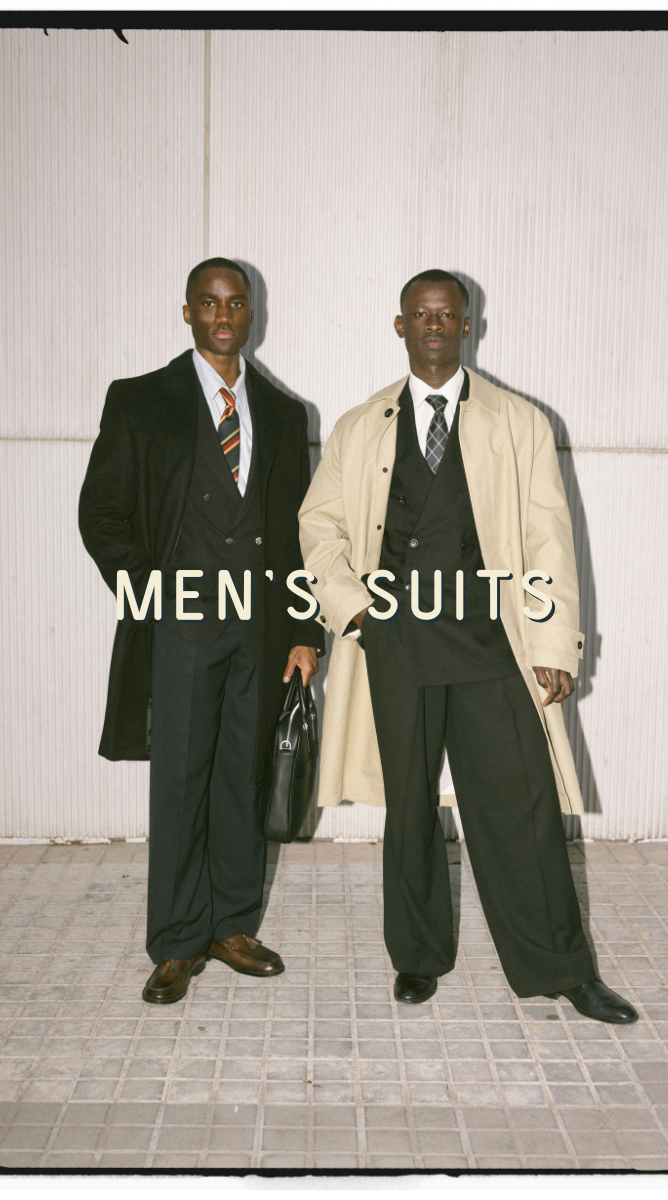 two men in black suits and overcoats in a fashion high flash photo. Caption: "Men's Suits"