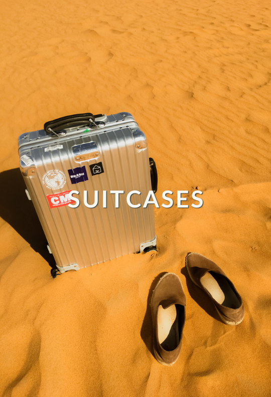 A silver suitcase and a pair of sandals on desert sand